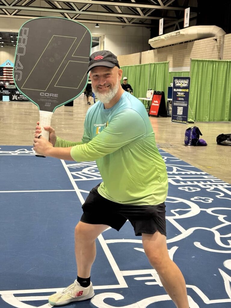 Dave Martin posing with an oversized novelty pickleball paddle at PickleCon