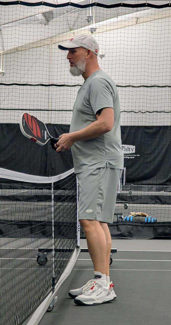 Dave Martin, pickleball coach and Selkirk Advocate, holding a Selkirk paddle at the net on an indoor pickleball court