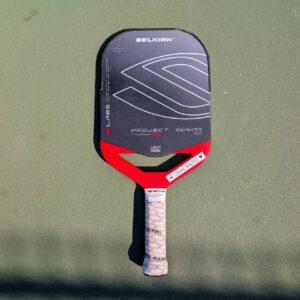 Selkirk LABS Project 007 Invikta pickleball paddle with aero handle, red and black, on a pickleball court