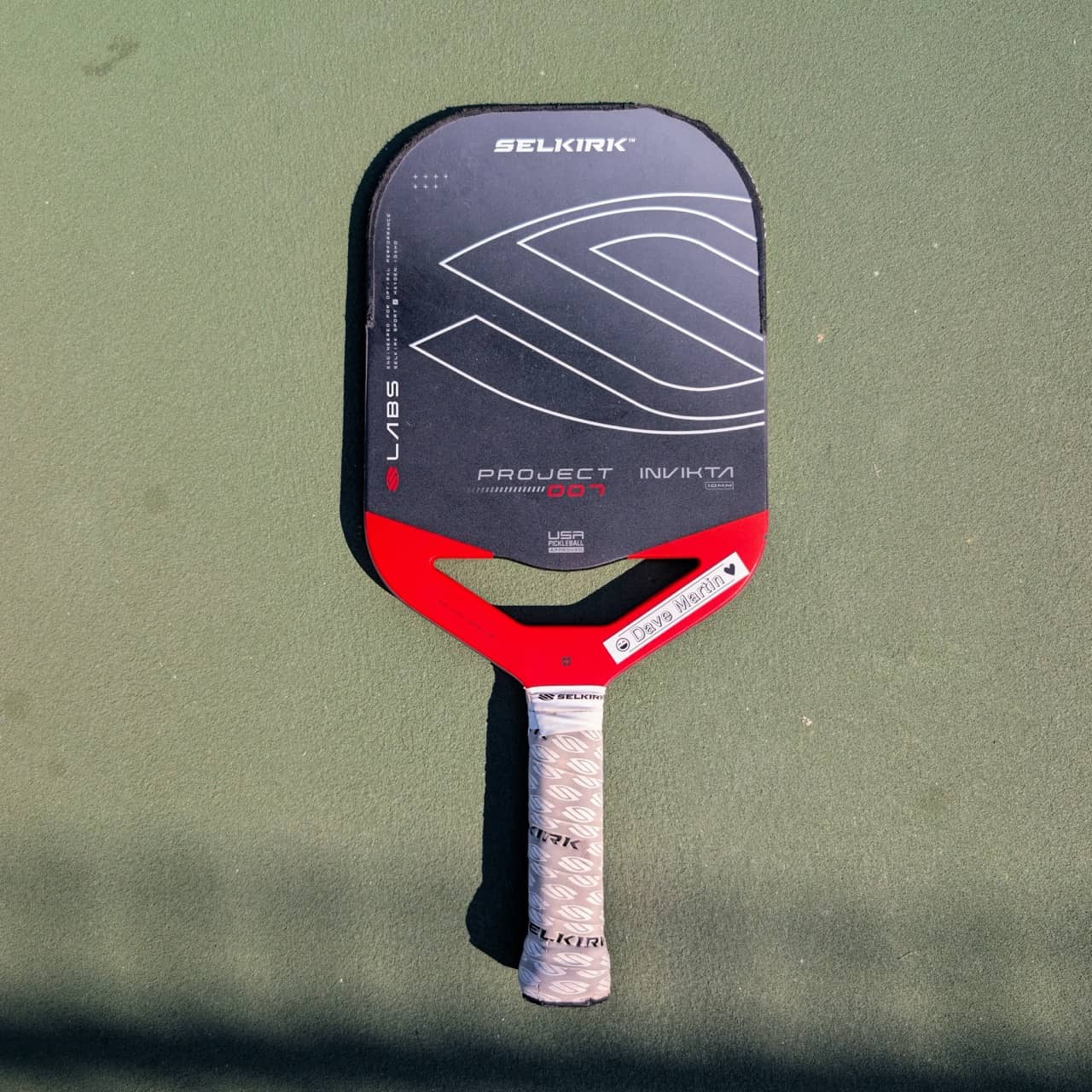 Selkirk LABS Project 007 Invikta pickleball paddle with aero handle, red and black, on a pickleball court