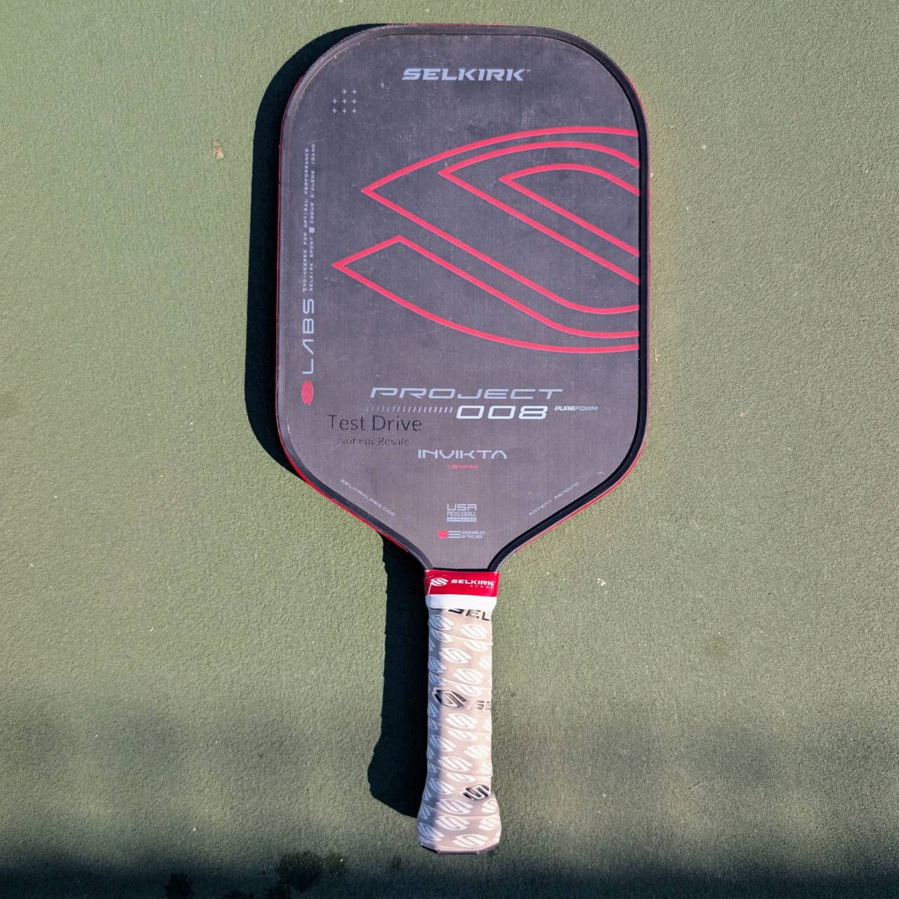 Selkirk LABS Project 008 pickleball paddle, PureForm, Invikta face, red and black, on a pickleball court