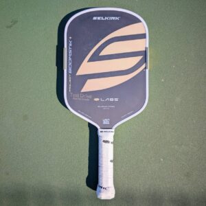Selkirk LABS Project Boomstik pickleball paddle, elongated shape, tan and gray, on a pickleball court