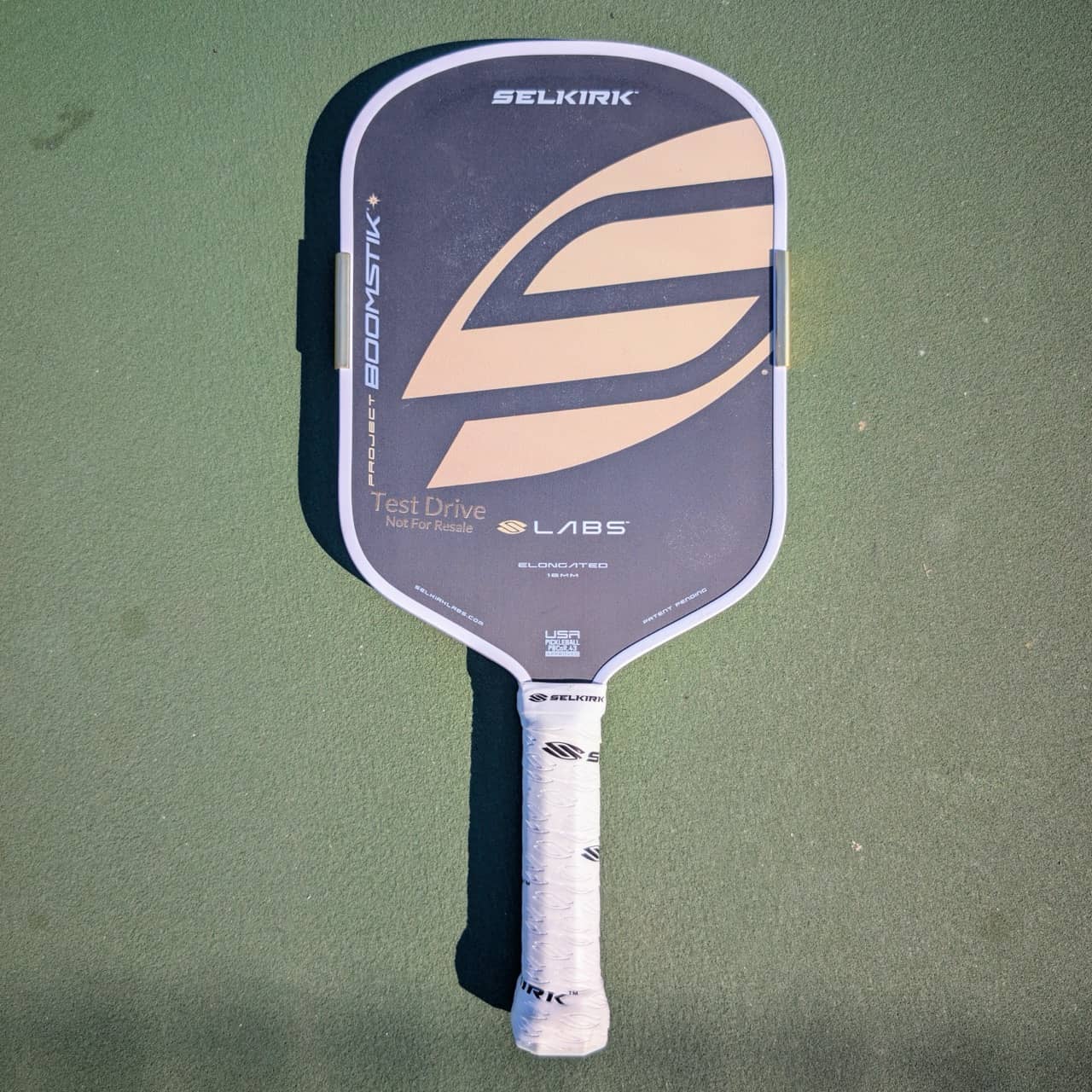 Selkirk LABS Project Boomstik pickleball paddle, elongated shape, tan and gray, on a pickleball court