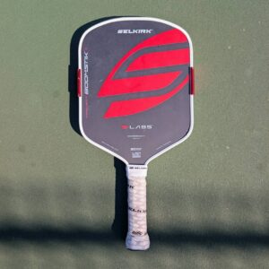 Selkirk LABS Project Boomstik pickleball paddle, widebody shape, red and gray, on a pickleball court