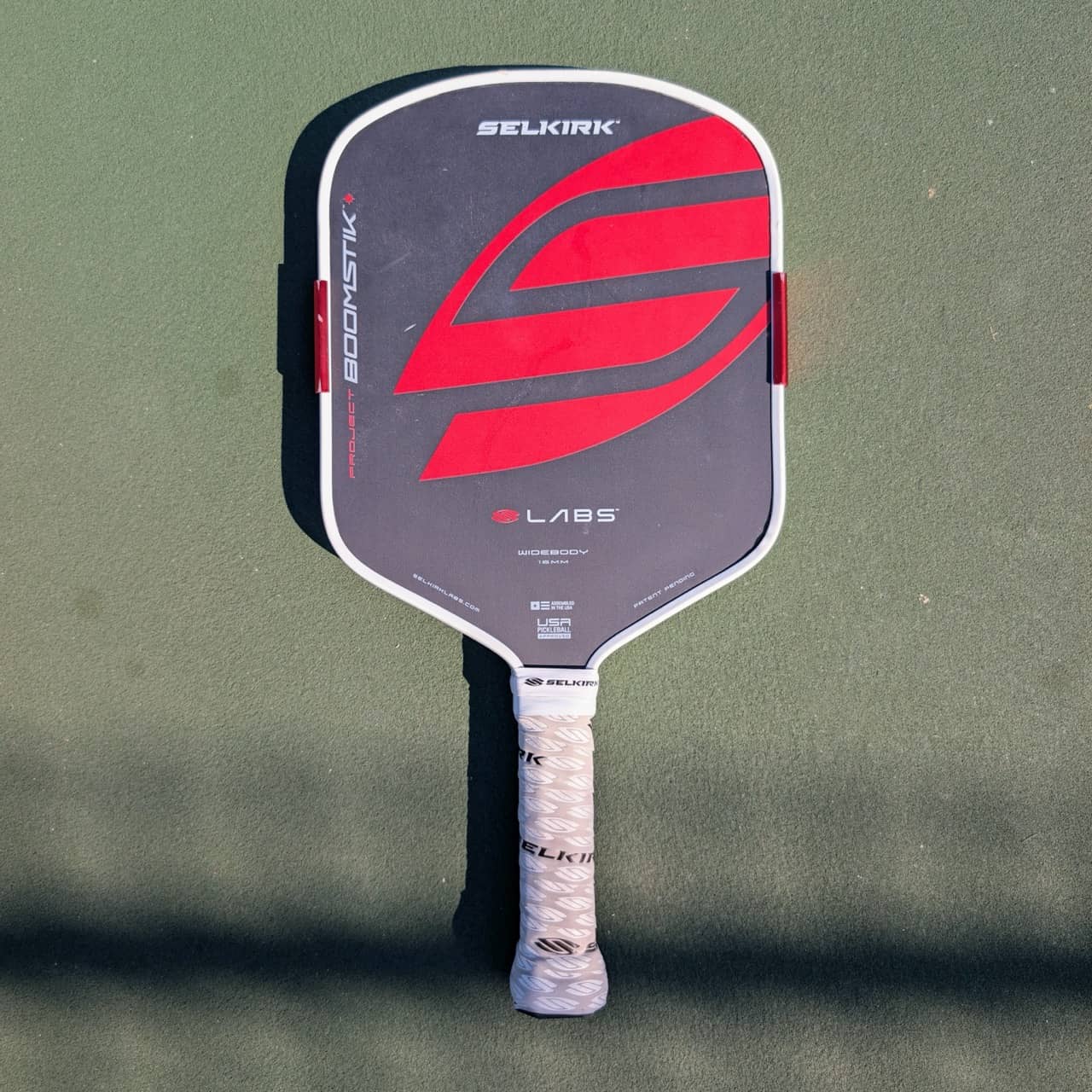 Selkirk LABS Project Boomstik pickleball paddle, widebody shape, red and gray, on a pickleball court