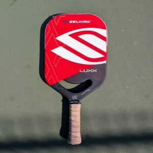 Selkirk LUXX Control Air pickleball paddle with aero handle, red and white, on a pickleball court