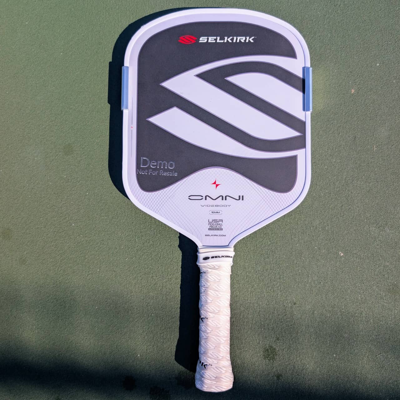 Selkirk Omni pickleball paddle, widebody shape, white and gray, on a pickleball court