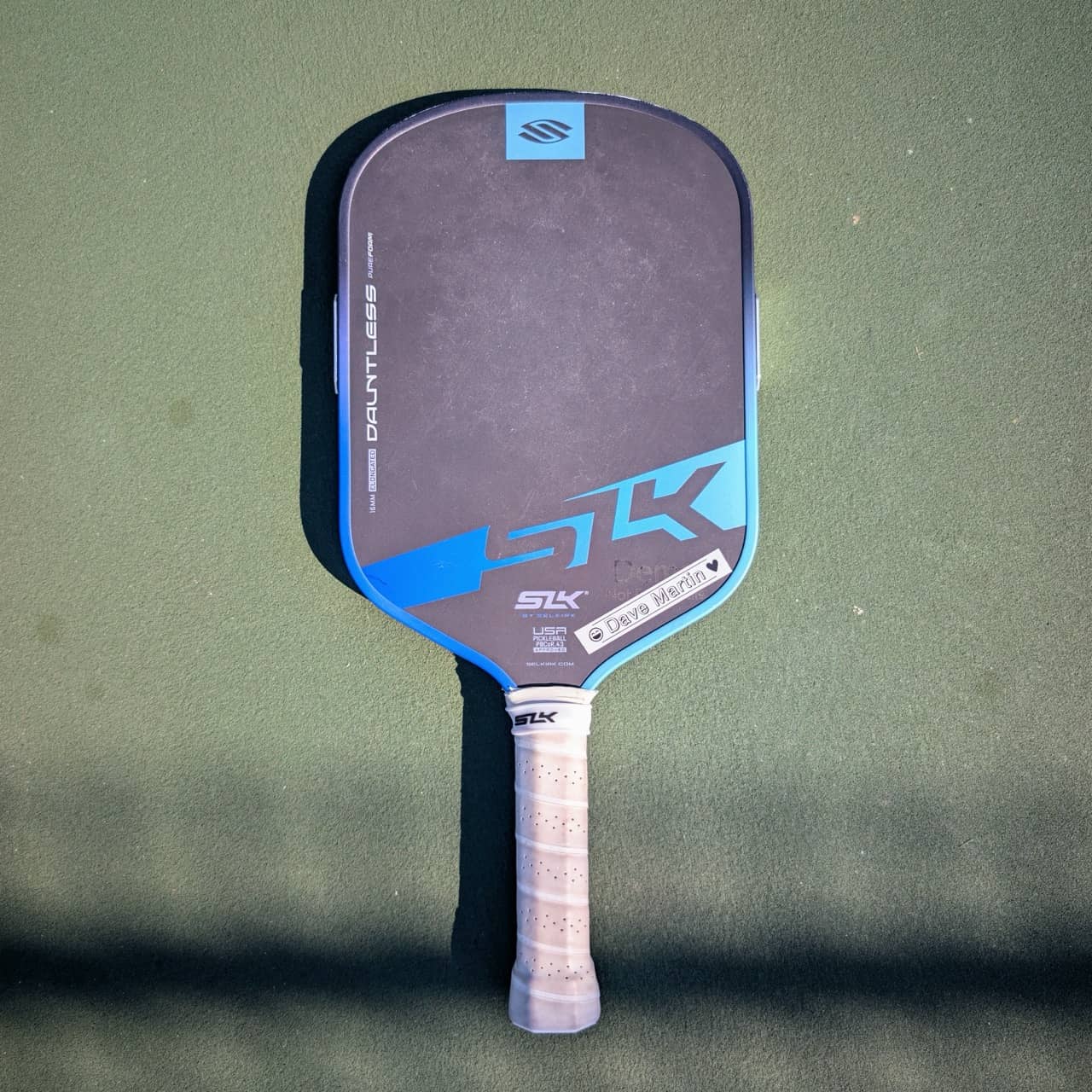Selkirk SLK Dauntless PureForm pickleball paddle, elongated shape, blue, on a pickleball court