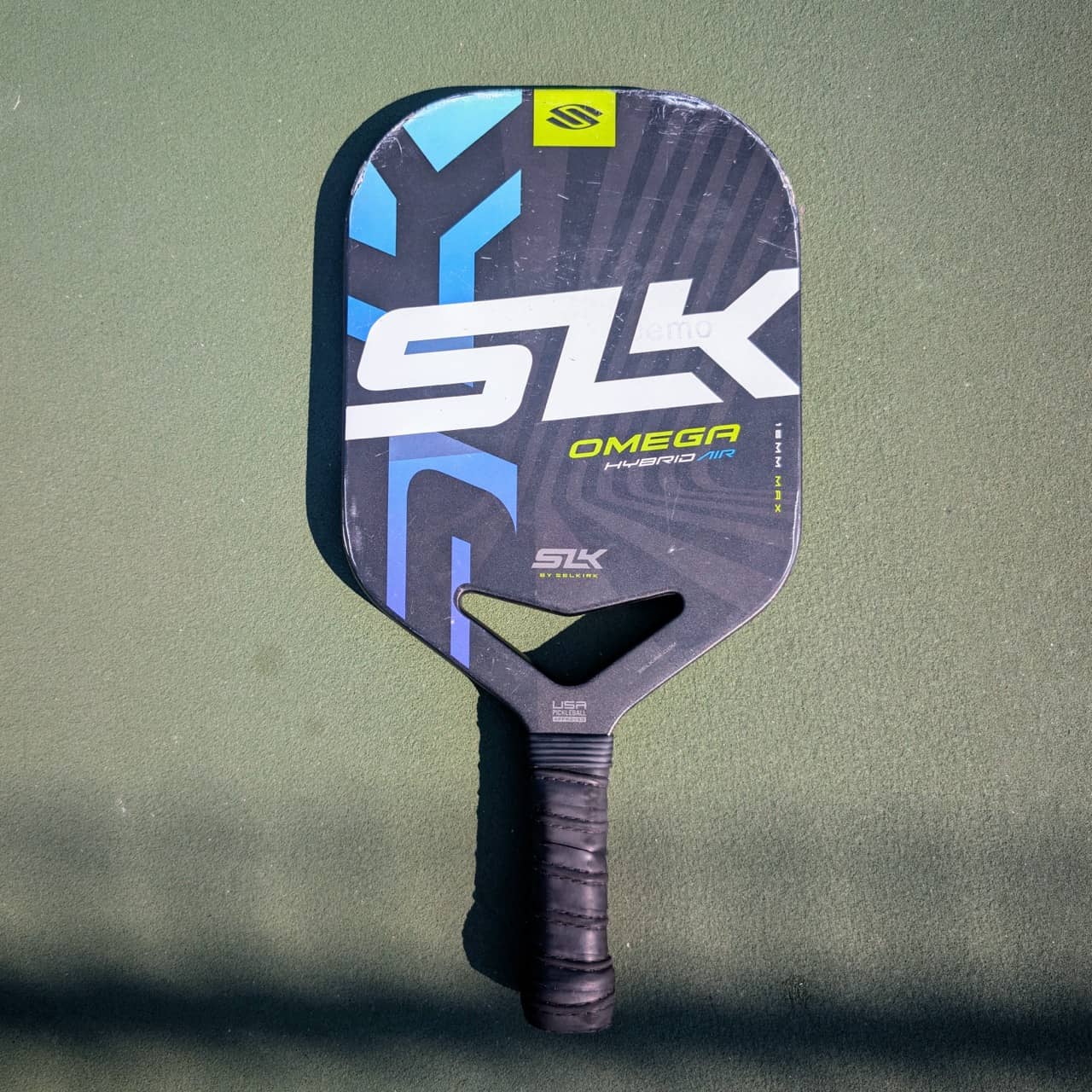Selkirk SLK Omega Hybrid Air pickleball paddle with aero handle, blue and black, on a pickleball court
